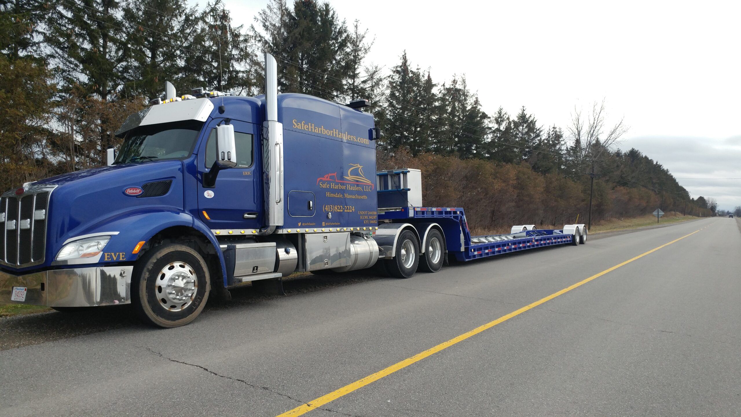 Safe Harbor Haulers blue Peterbilt truck with an empty lowboy trailer, ready for boat transport on an open highway.